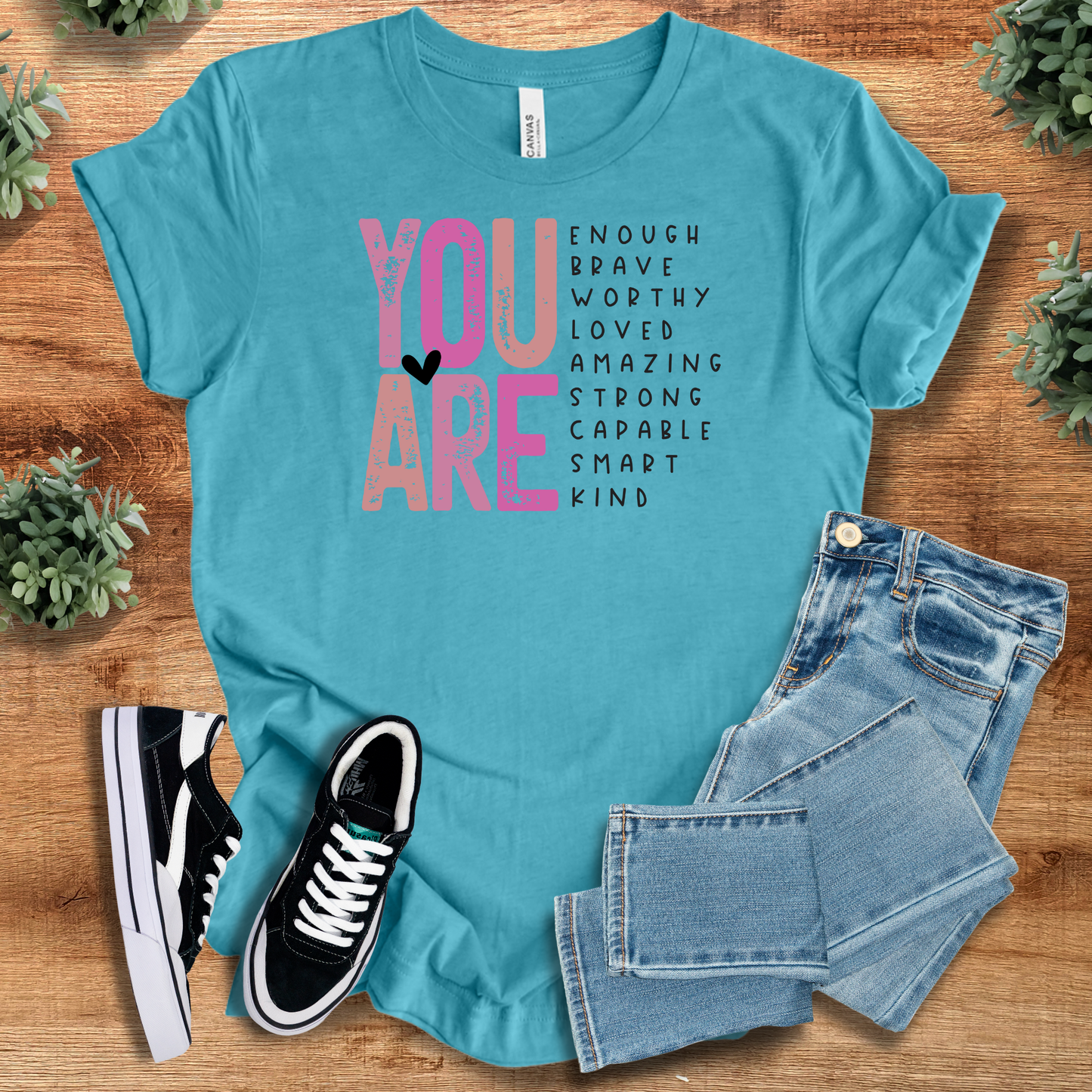 White t-shirt with '' text, flat lay styled on a wooden surface.