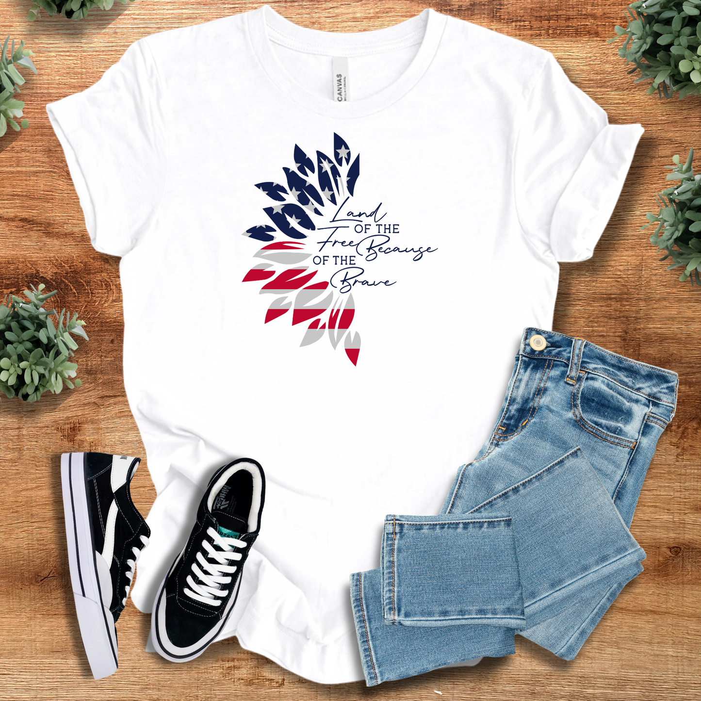 White t-shirt with 'Sunflower Flag Land Of The Free T‑Shirt' text, flat lay styled on a wooden surface.