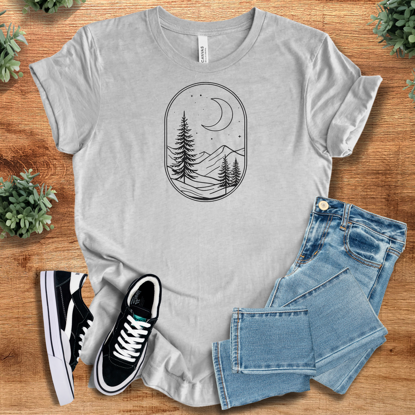 Athletic-heather t-shirt with 'Woodsy Moon T‑Shirt' text, flat lay styled on a wooden surface.