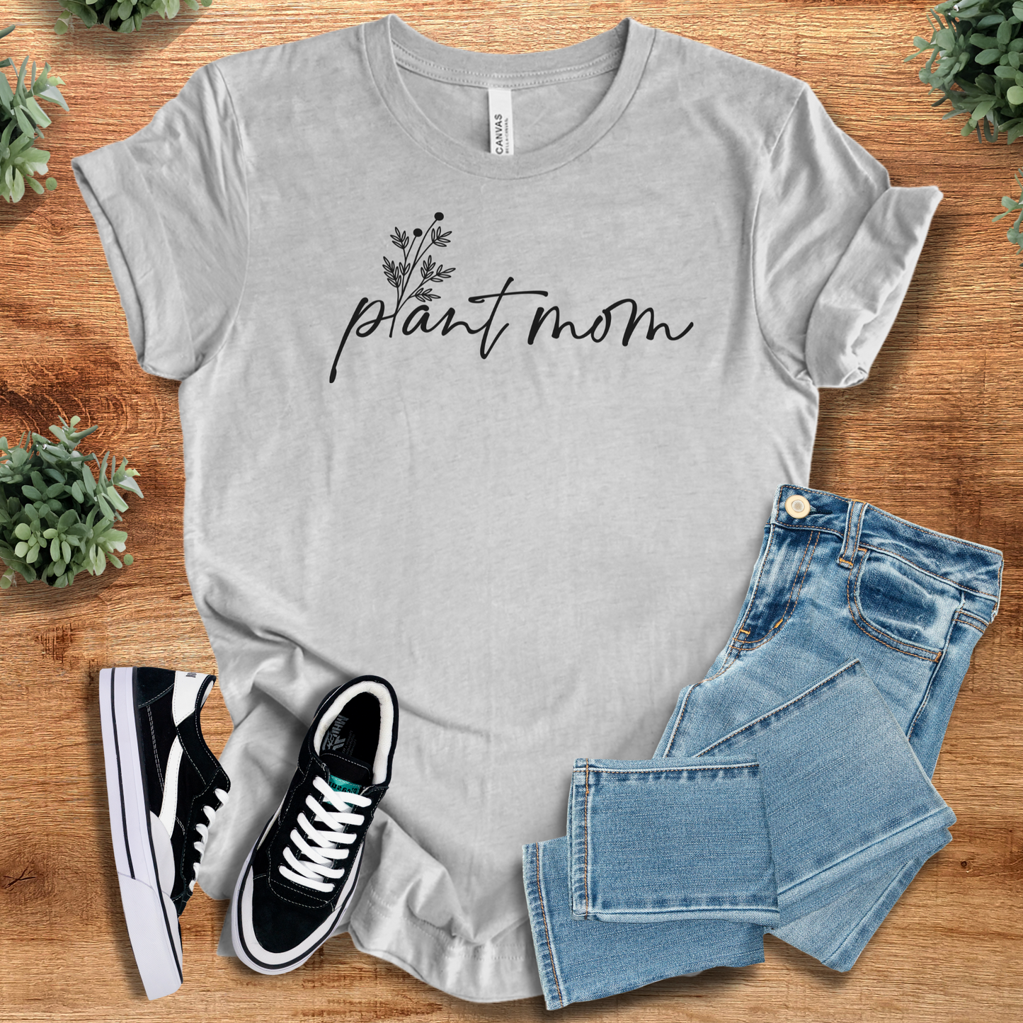 Military-green t-shirt with '' text, flat lay styled on a wooden surface.