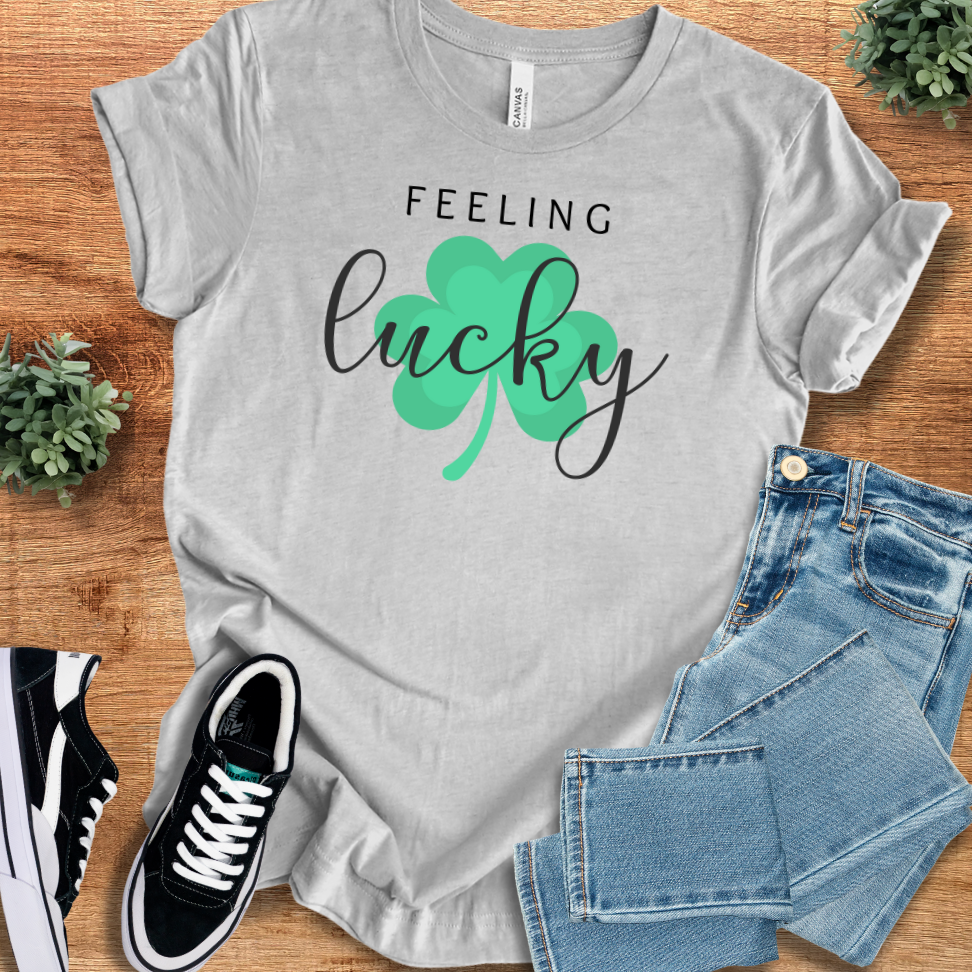 Athletic Heather t-shirt with 'Feeling Lucky T‑Shirt' text, flat lay styled on a wooden surface.