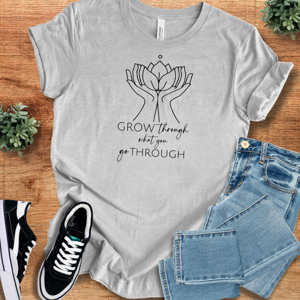 Athletic-heather t-shirt with 'Grow Thru What You Go Thru T‑Shirt' text, flat lay styled on a wooden surface.