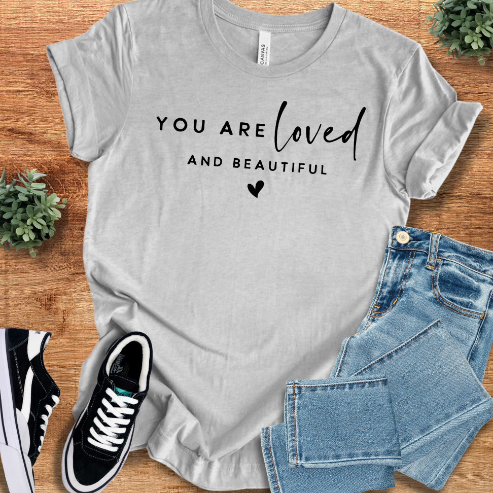 Athletic-heather t-shirt with 'You Are Loved T‑Shirt' text, flat lay styled on a wooden surface.