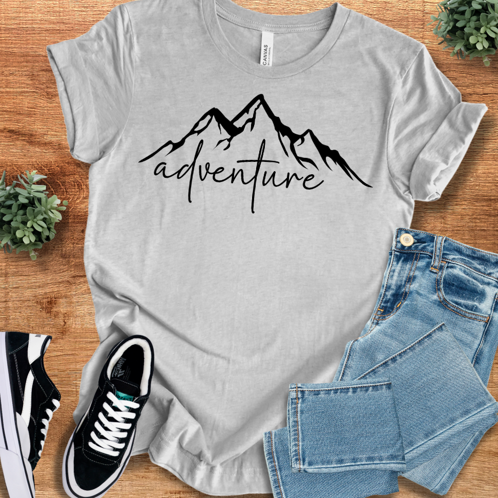 Athletic-heather t-shirt with 'Mountain Adventure T‑Shirt' text, flat lay styled on a wooden surface.