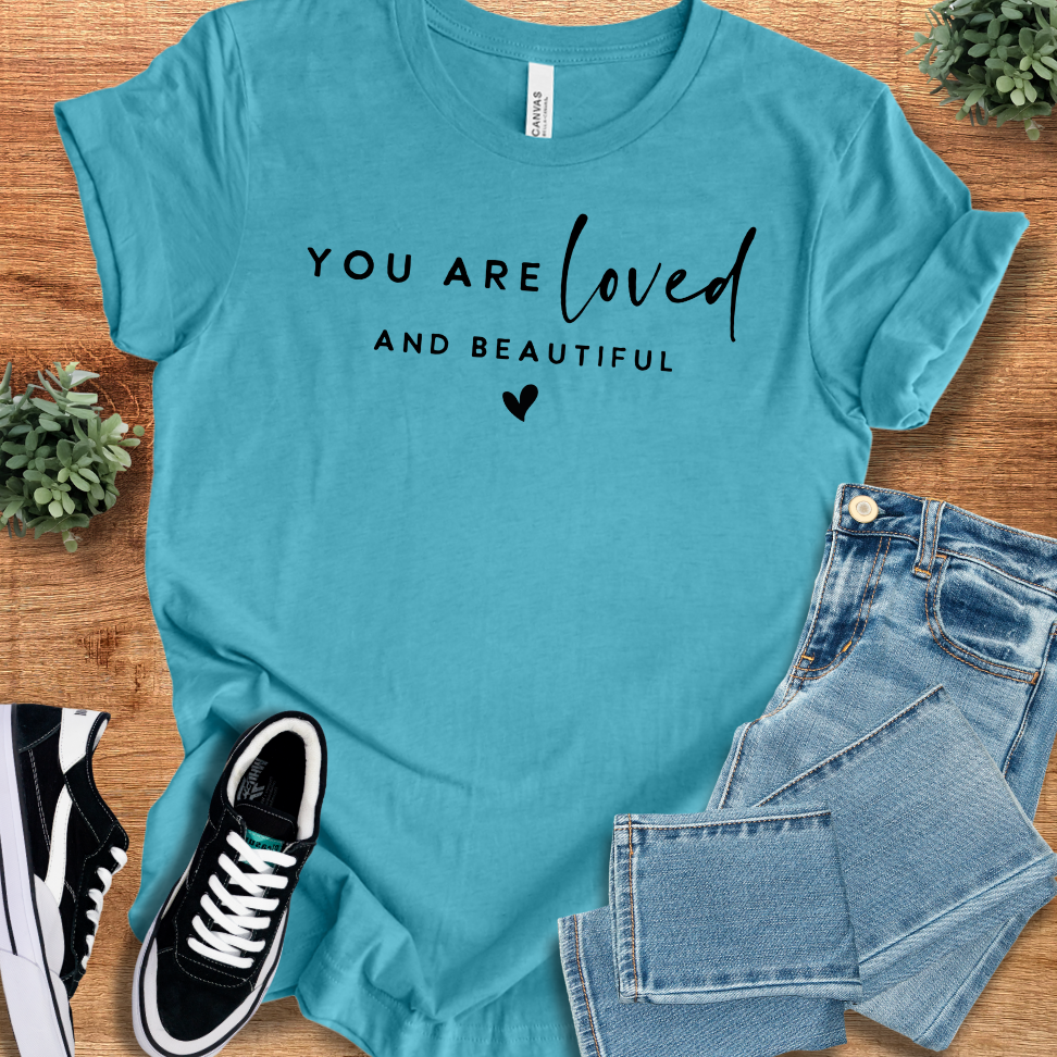 Heather-aqua t-shirt with '' text, flat lay styled on a wooden surface.