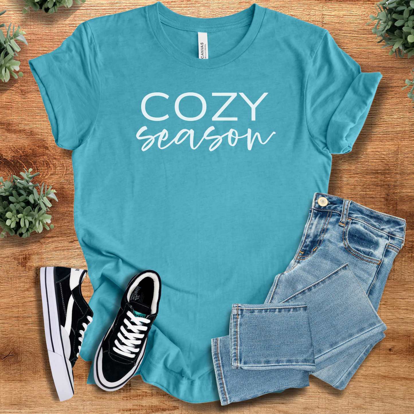 Heather-aqua t-shirt with 'Cozy Season T‑Shirt' text, flat lay styled on a wooden surface.