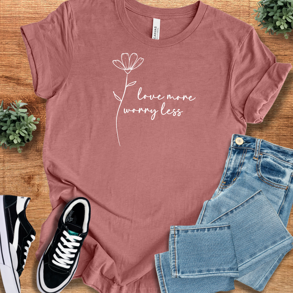 Heather-mauve t-shirt with 'Love More, Worry Less T‑Shirt' text, flat lay styled on a wooden surface.