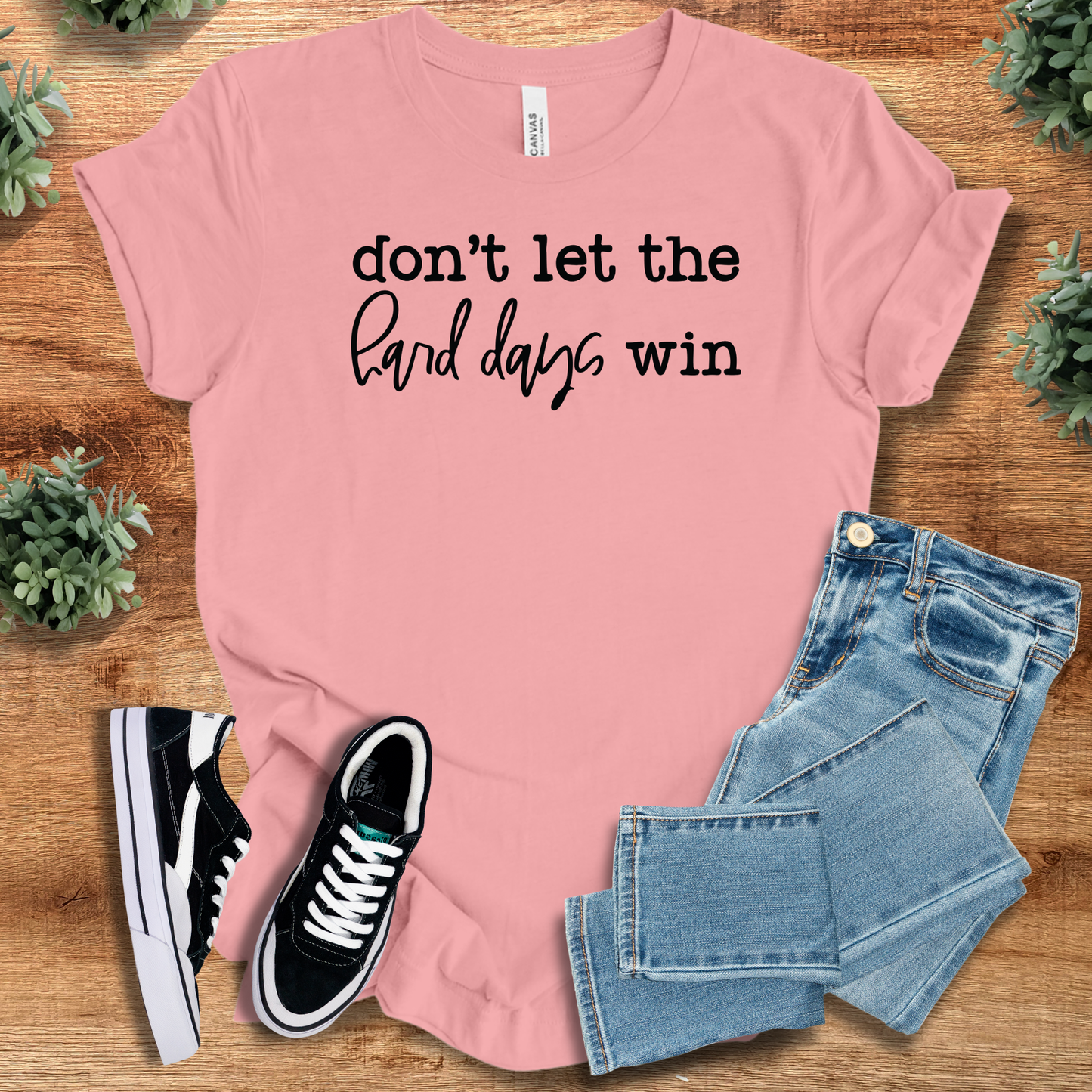 Light pink Don't Let Hard Days Win cotton T-Shirt with black text, styled for a soft, empowering look in casual wellness fashion.
