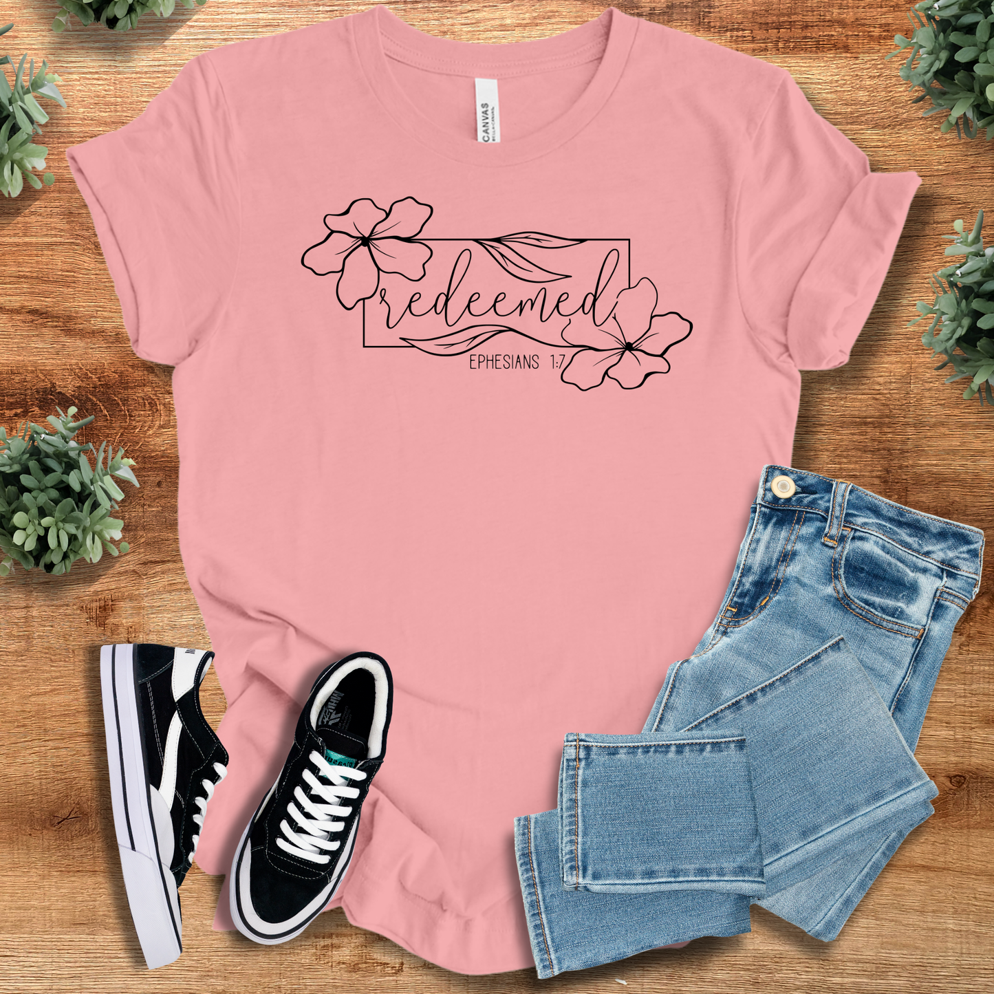 Light pink Redeemed Ephesians 1:7 Christian T-shirt with floral design, adult fit cotton tee, styled with jeans and casual shoes on wood.
