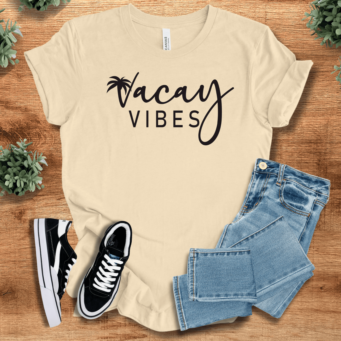 Soft-cream t-shirt with 'Vacay Vibes T‑Shirt' text, flat lay styled on a wooden surface.