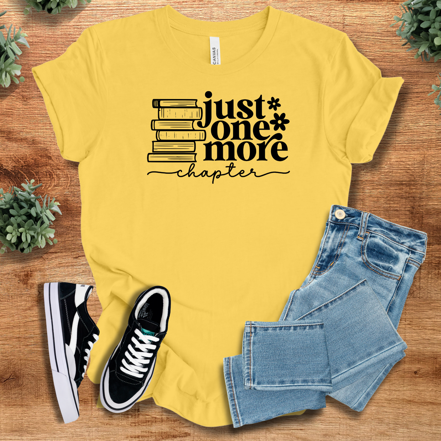 Bright yellow 'Just One More Chapter' book lover's t-shirt with black text and book stack. Fun unisex tee for reading enthusiasts.