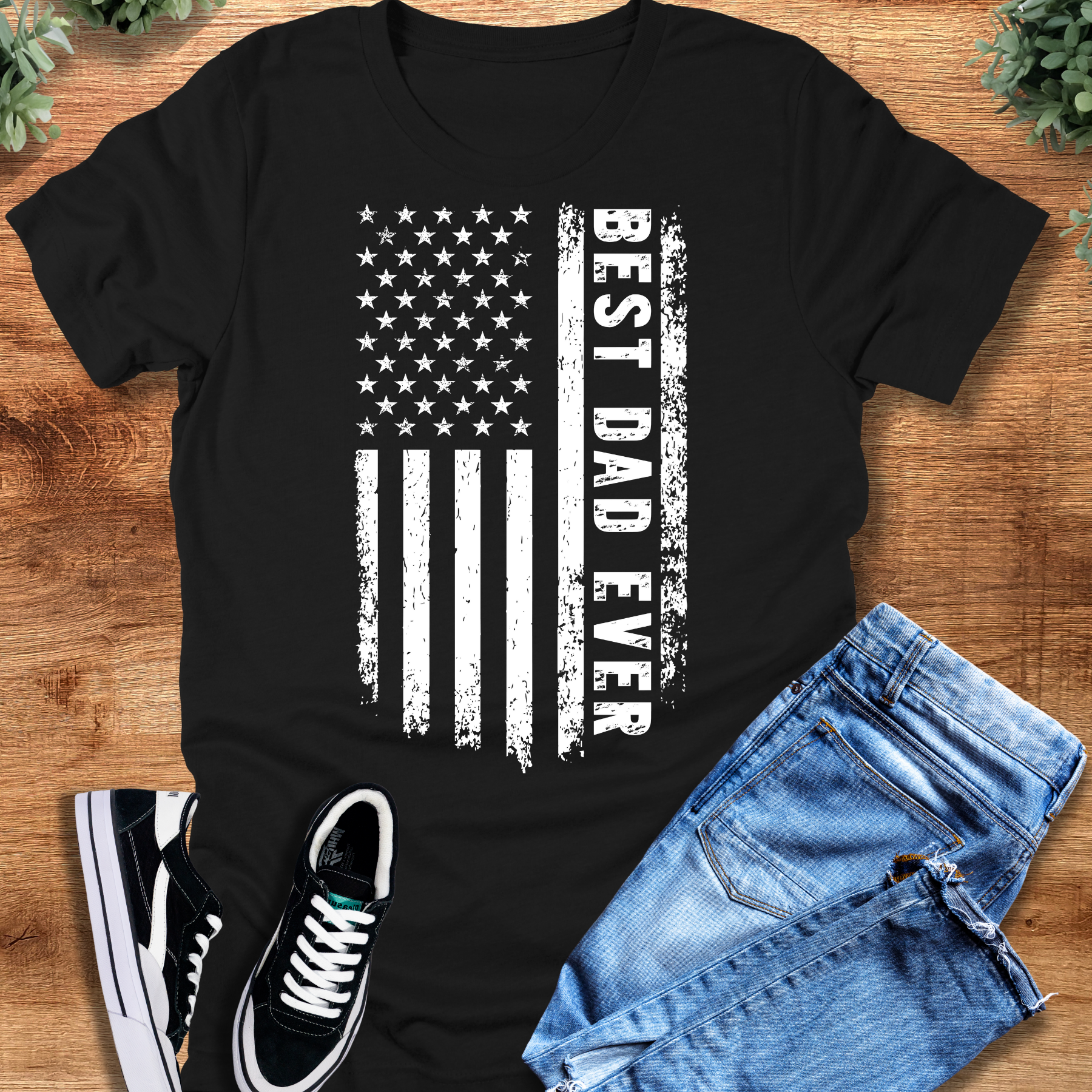 Black t-shirt with 'Best Dad Ever Flag T‑Shirt' text, flat lay styled on a wooden surface.