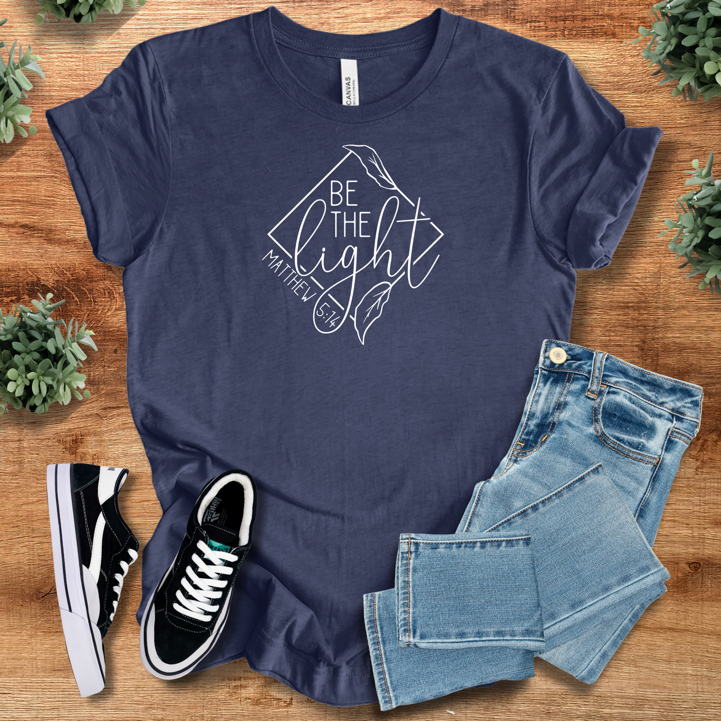 Navy Be the Light Matthew 5:14 T-shirt with white script and leaf motif, styled with casual denim and shoes for religious wear.