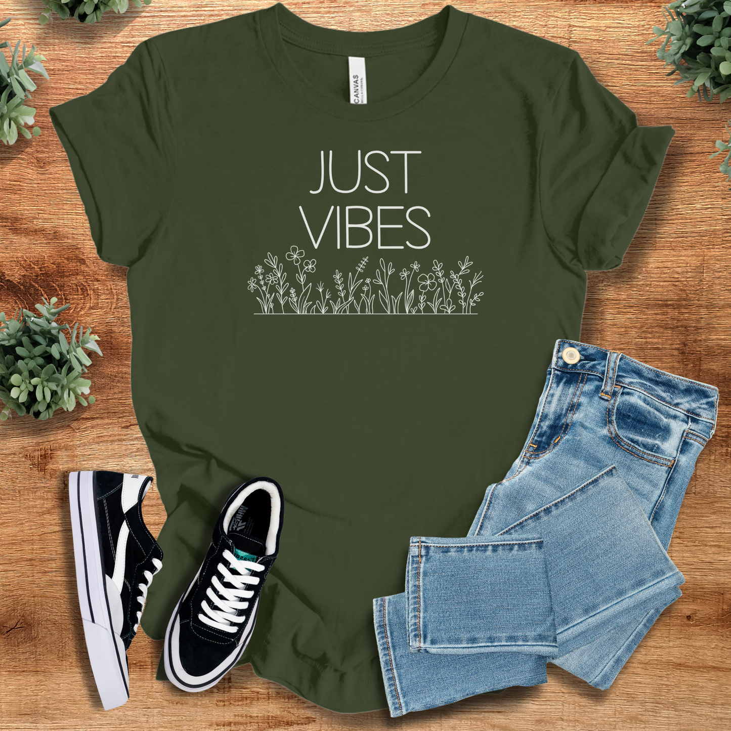 Olive green Just Vibes Wildflower T‑Shirt crafted from Bella+Canvas 3001. Soft unisex tee with nature graphic, styled with denim and sneakers.