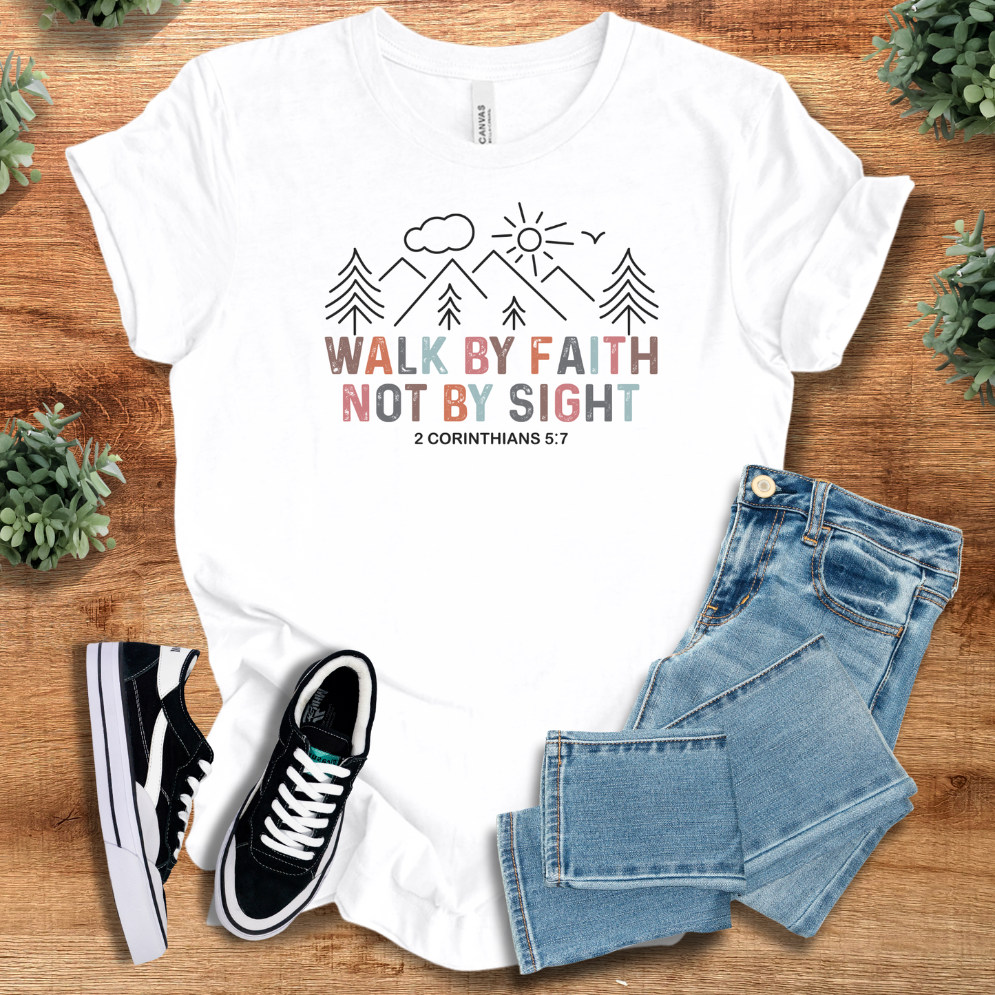 White t-shirt with motivational quote, black and white sneakers, and blue jeans on a wooden surface.