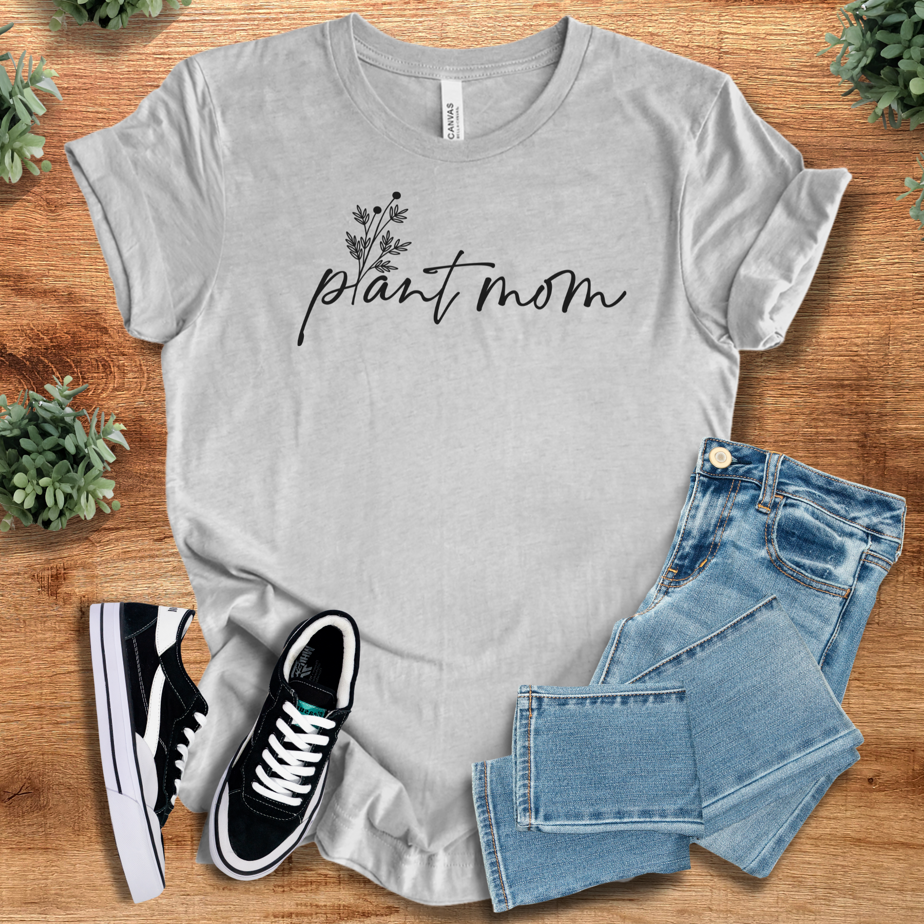 Military-green t-shirt with '' text, flat lay styled on a wooden surface.