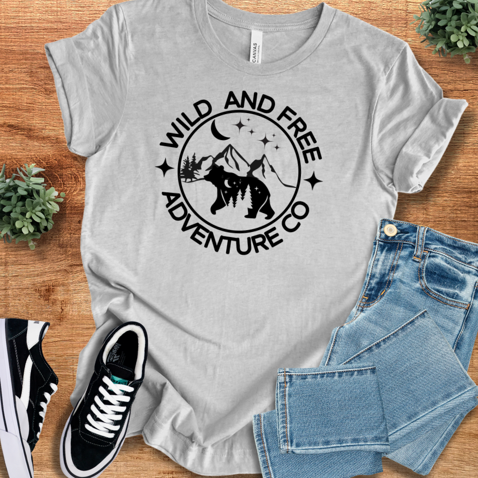 Light gray adventure t-shirt with 'Wild And Free Adventure Co' bear and mountain design. Breathable, sustainable fabric, ideal for outdoor activities and everyday wear.
