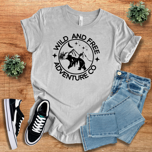 Light gray adventure t-shirt with 'Wild And Free Adventure Co' bear and mountain design. Breathable, sustainable fabric, ideal for outdoor activities and everyday wear.