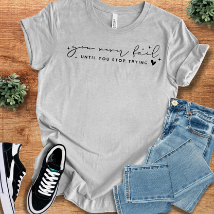 Athletic-heather t-shirt with 'You Never Fail Until T‑Shirt' text, flat lay styled on a wooden surface.