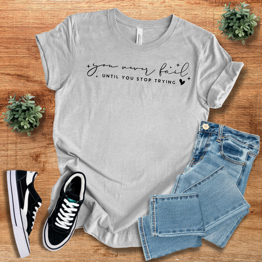 Gray 'You Never Fail Until You Stop Trying' motivational t-shirt with black script text. Soft cotton, unisex fit, perfect for casual wear.