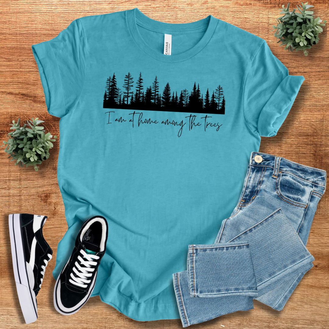 Turquoise nature lover T-shirt featuring a black forest silhouette and 'I'm At Home Among The Trees' text. A vibrant and comfortable outdoor tee.