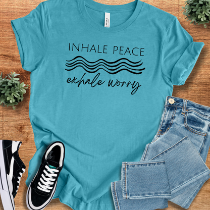Heather-aqua t-shirt with 'Inhale Peace Exhale Worry T‑Shirt' text, flat lay styled on a wooden surface.