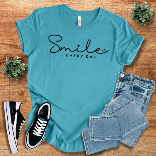 Turquoise 'Smile Every Day' t-shirt with black script, styled with denim jeans and sneakers. Soft cotton, unisex fit, perfect for casual wear.