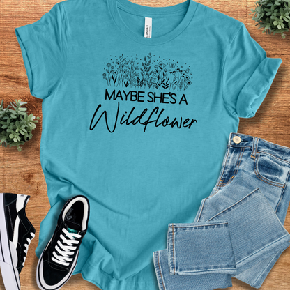 Heather-aqua t-shirt with 'Maybe She's A Wildflower T‑Shirt' text, flat lay styled on a wooden surface.