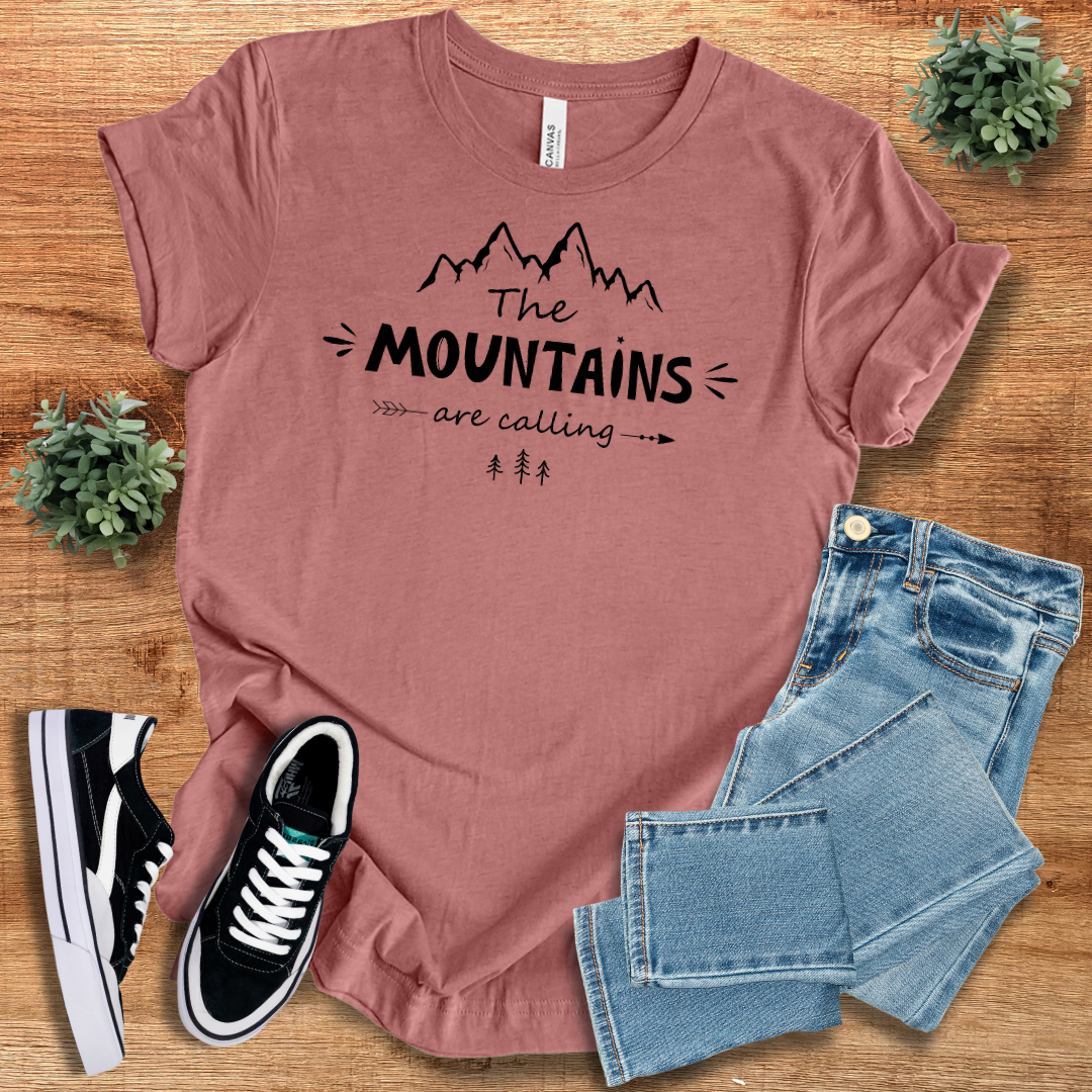 Dusty rose 'The Mountains Are Calling' T-shirt with black mountain print. Trendy and comfortable outdoor adventure tee for nature lovers.