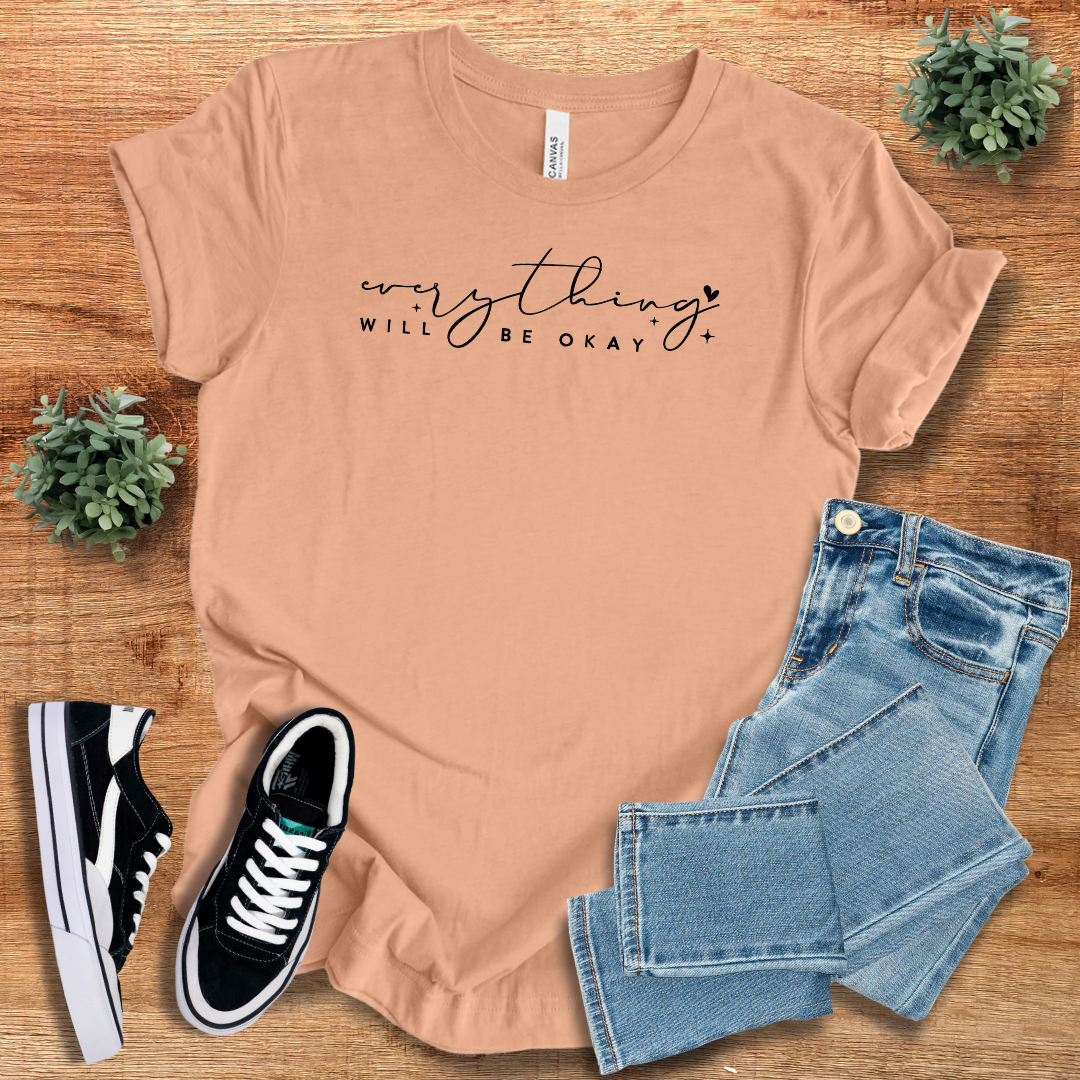 Peach 'Everything Will Be Ok' t-shirt with black script text, styled with denim jeans and sneakers. A soft and breathable cotton casual tee.