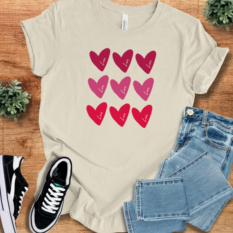 Cream-colored Bella+Canvas Valentine Hearts T‑Shirt with red and pink heart graphics, soft unisex tee for romantic or casual wear.