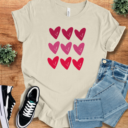 Cream-colored Bella+Canvas Valentine Hearts T‑Shirt with red and pink heart graphics, soft unisex tee for romantic or casual wear.