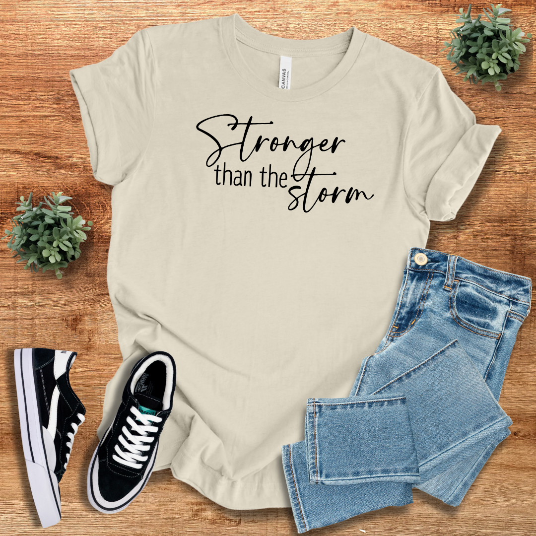 Off-white Stronger Than The Storm T-Shirt featuring black script text, paired with jeans and sneakers for a minimalist, empowering outfit.