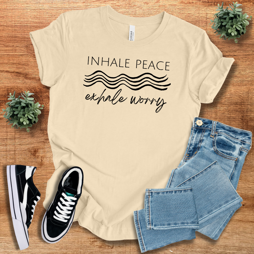 Beige 'Inhale Peace Exhale Worry' t-shirt with black script design. Sustainable cotton, crew neck, and unisex fit for a relaxed style.