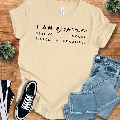 Soft-cream t-shirt with 'I Am Woman T‑Shirt' text, flat lay styled on a wooden surface.