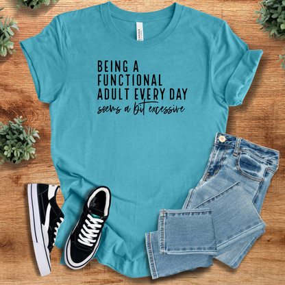 Heather-navy t-shirt with 'Being A Functional Adult Everyday Seems A Bit Excessive T‑Shirt' text, flat lay styled on a wooden surface.