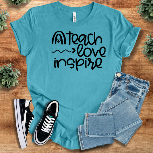 Aqua blue Teach Love Inspire Tee with bold black lettering, styled with jeans and sneakers. Perfect unisex inspirational teacher shirt.
