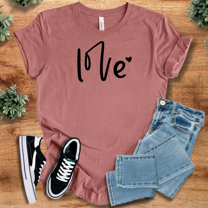Pink t-shirt with '' text, flat lay styled on a wooden surface.