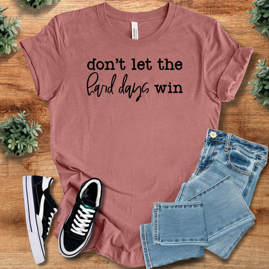 Inspirational T-Shirt Don't Let Hard Days Win in mauve cotton with black text, styled with jeans and sneakers for casual empowerment wear.