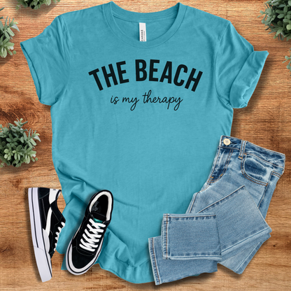 Heather-aqua t-shirt with 'The Beach Is My Therapy T‑Shirt' text, flat lay styled on a wooden surface.