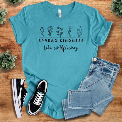 Heather-aqua t-shirt with 'Spread Kindness With Wildflowers T‑Shirt' text, flat lay styled on a wooden surface.