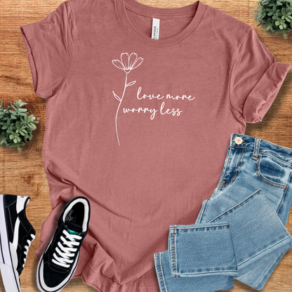 Heather-mauve t-shirt with 'Love More, Worry Less T‑Shirt' text, flat lay styled on a wooden surface.