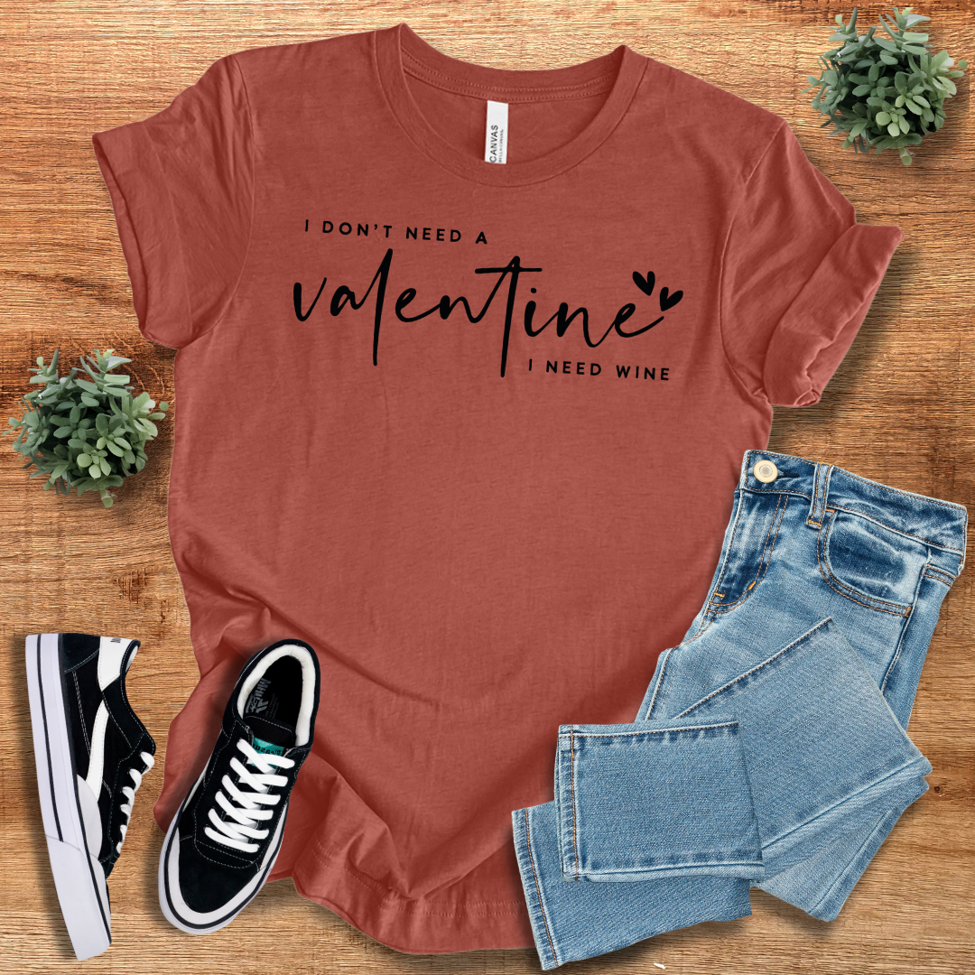 Rust-colored 'I Don’t Need a Valentine, I Need Wine' T-shirt with a bold black script design, paired with jeans and sneakers.