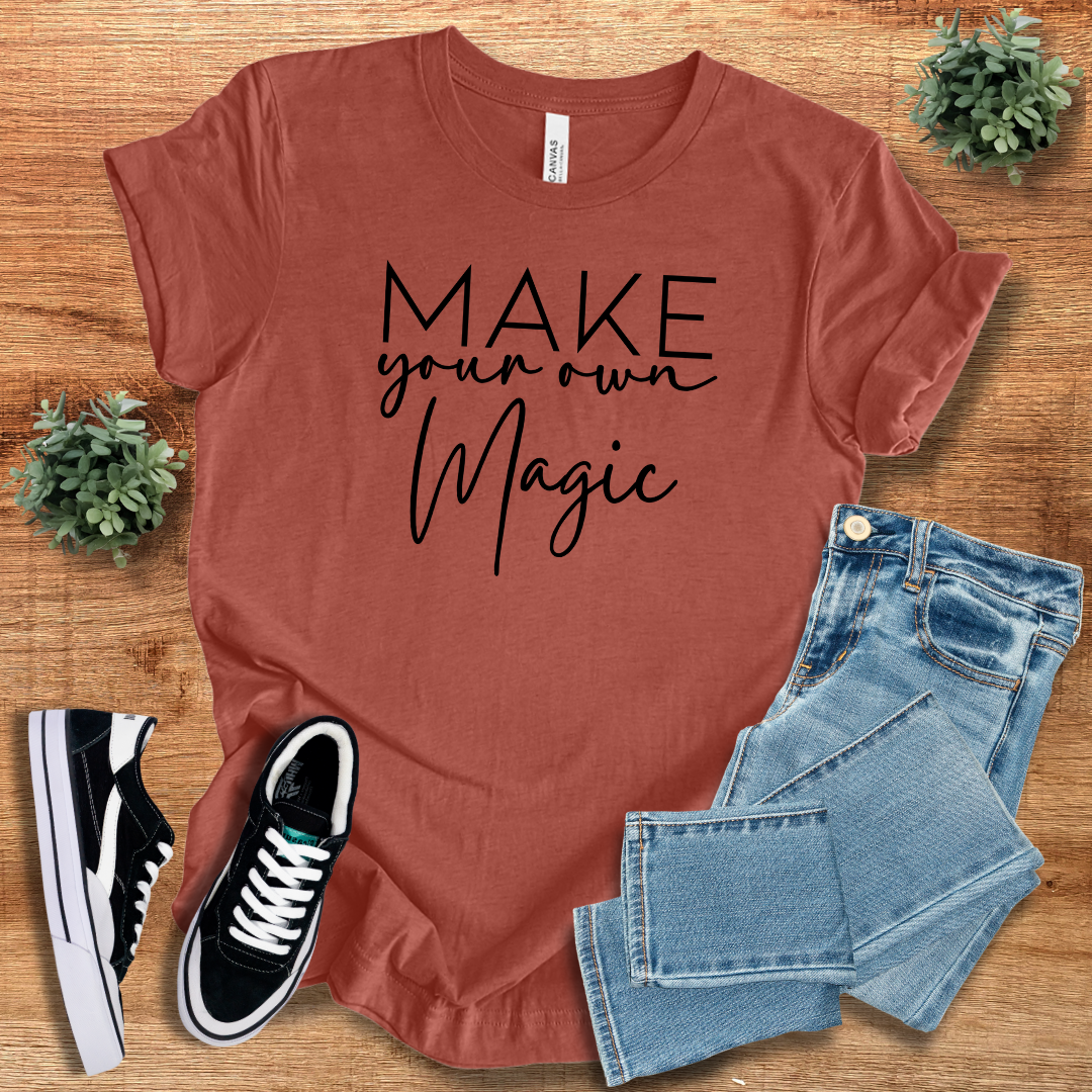 Rust-colored 'Make Your Own Magic' unisex t-shirt with black script text, paired with denim jeans and sneakers. Trendy, regular-fit cotton tee for casual outfits.