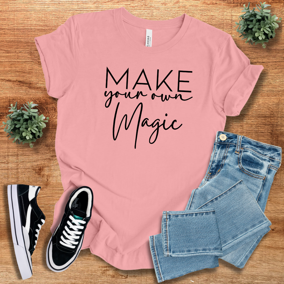 Pink 'Make Your Own Magic' unisex t-shirt with black script text, laid out with jeans and sneakers. Stylish, regular-fit cotton tee for casual and trendy outfits.