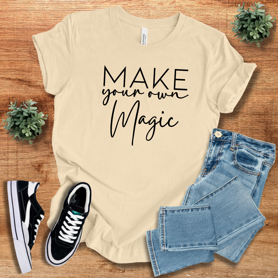 Cream 'Make Your Own Magic' unisex t-shirt with black script text, paired with denim jeans and sneakers. Soft, breathable cotton tee for everyday casual wear.