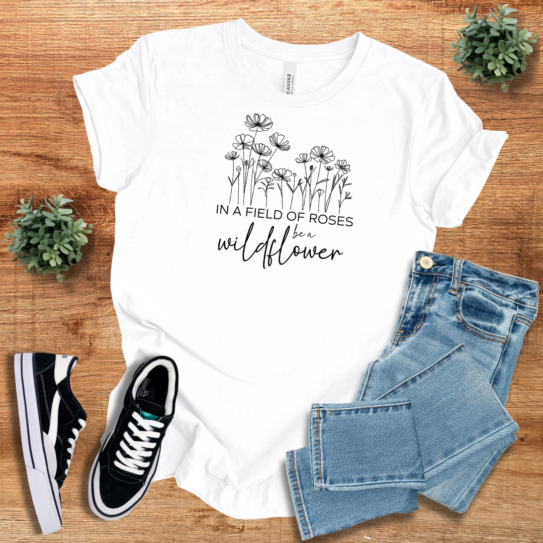 White 'In A Field Of Roses Be A Wildflower' t-shirt with floral graphic, casual crew neck, and breathable cotton fabric.