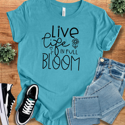 Heather-aqua t-shirt with 'Live Life In Full Bloom T‑Shirt' text, flat lay styled on a wooden surface.