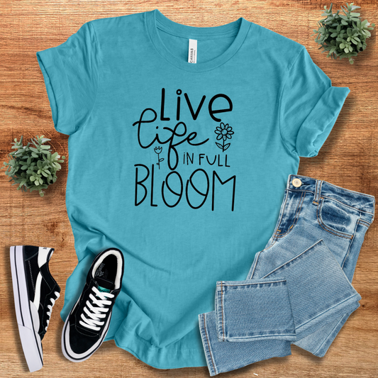 Turquoise 'Live Life in Full Bloom' t-shirt featuring black floral typography, paired with denim jeans and sneakers. A soft, breathable cotton tee for stylish everyday wear.