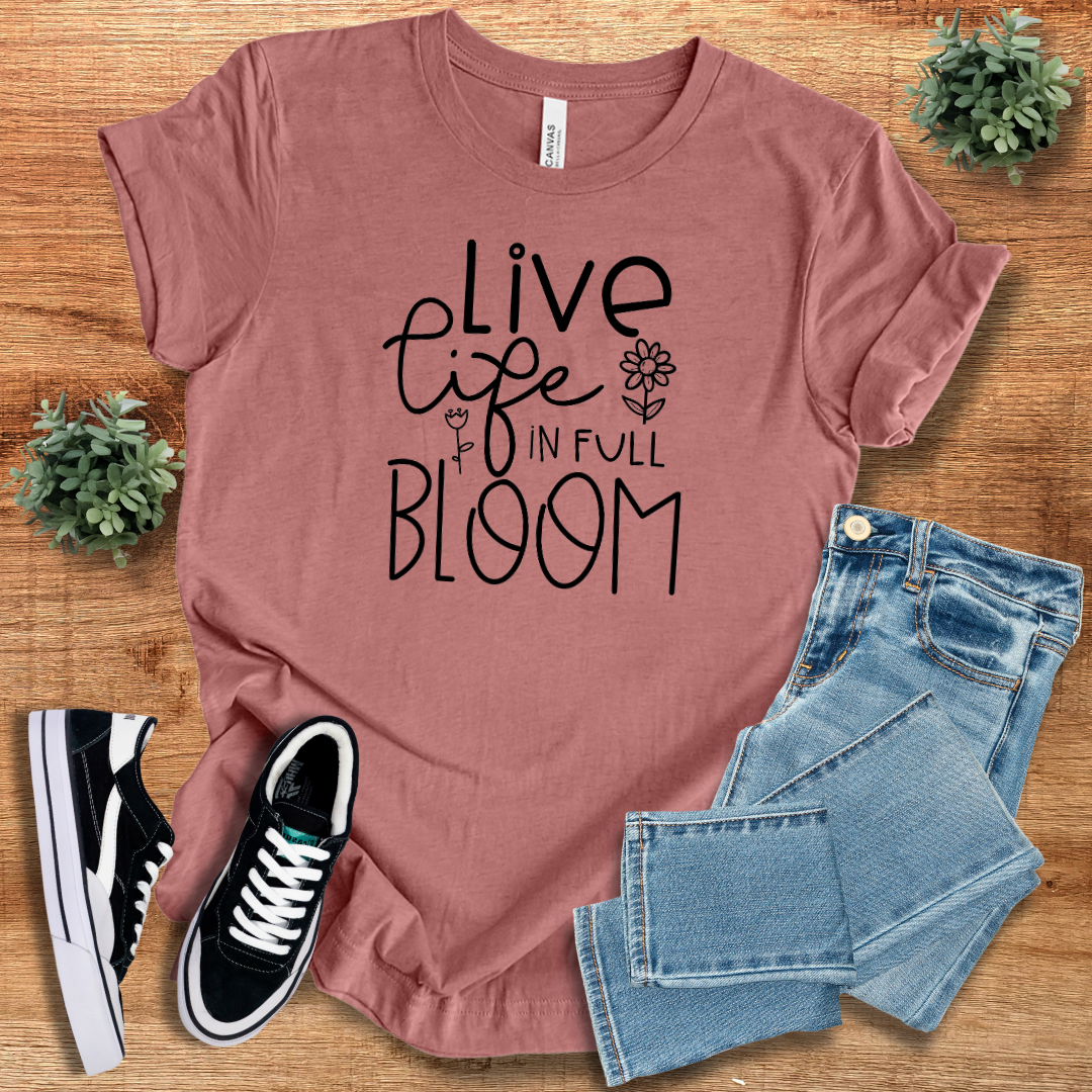 Mauve 'Live Life in Full Bloom' t-shirt with black floral typography, styled with denim jeans and sneakers. A sustainable, regular-fit cotton tee for casual fashion.